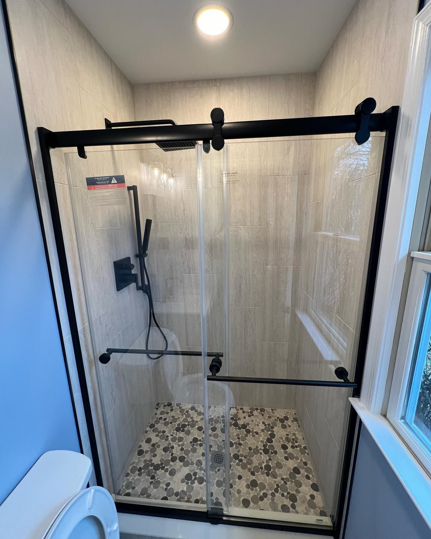 Shower with black frame, glass doors, pebble floor, and black showerhead.