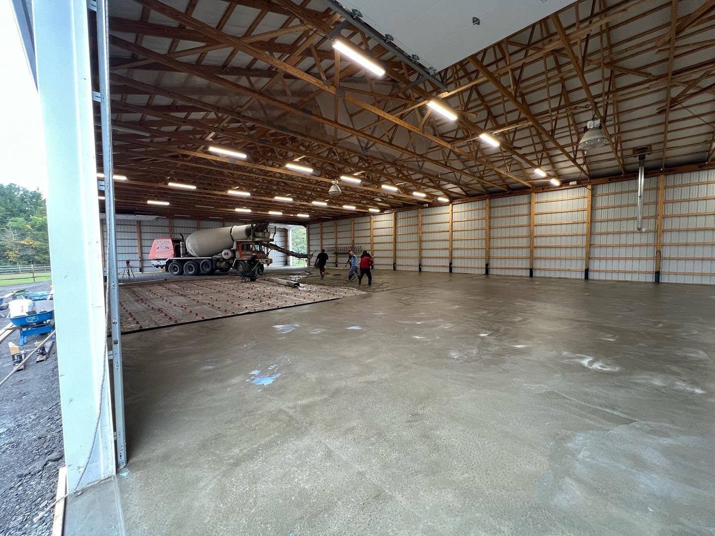 Concrete being poured inside a large warehouse. Several workers and a cement truck are present.
