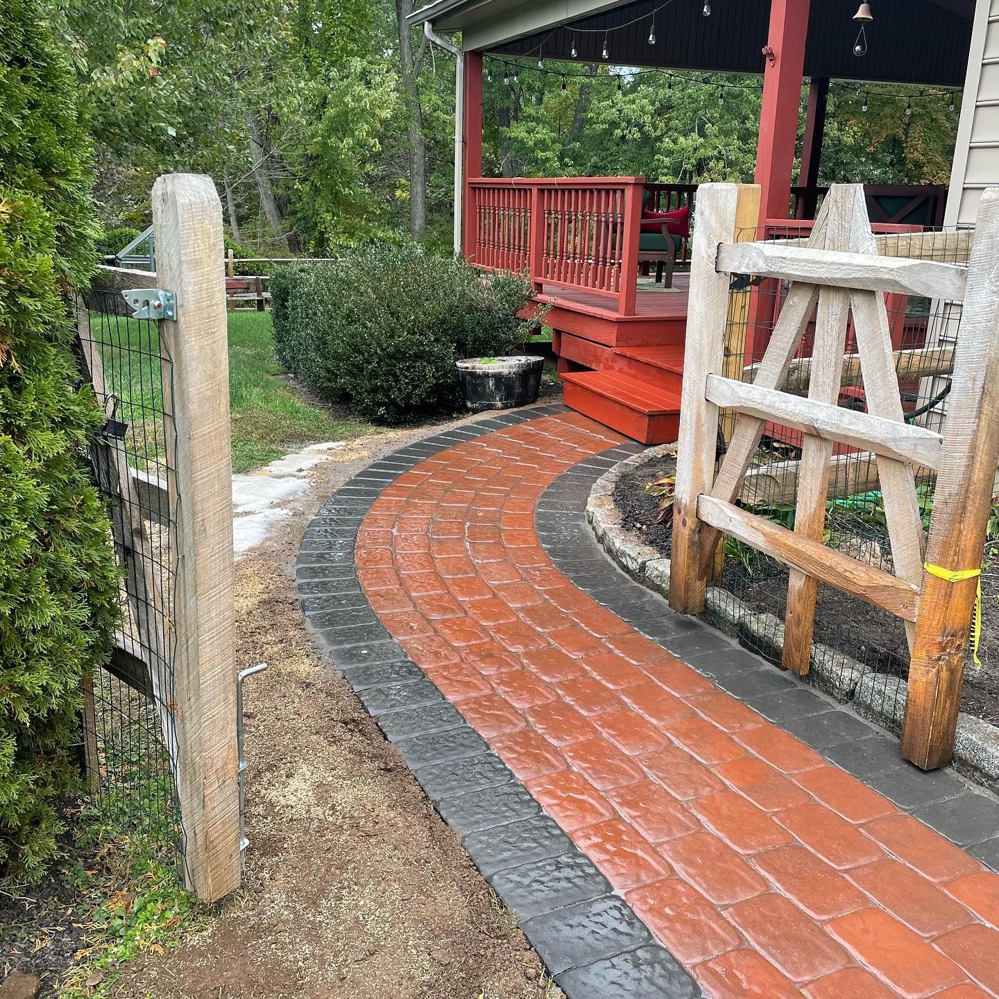 Brick walkway with wooden gates and porch leading to a red deck.