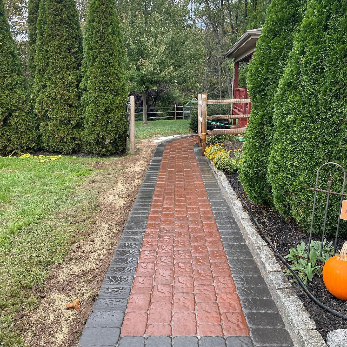 Brick path bordered by dark and red bricks, with trees and a fenced yard.