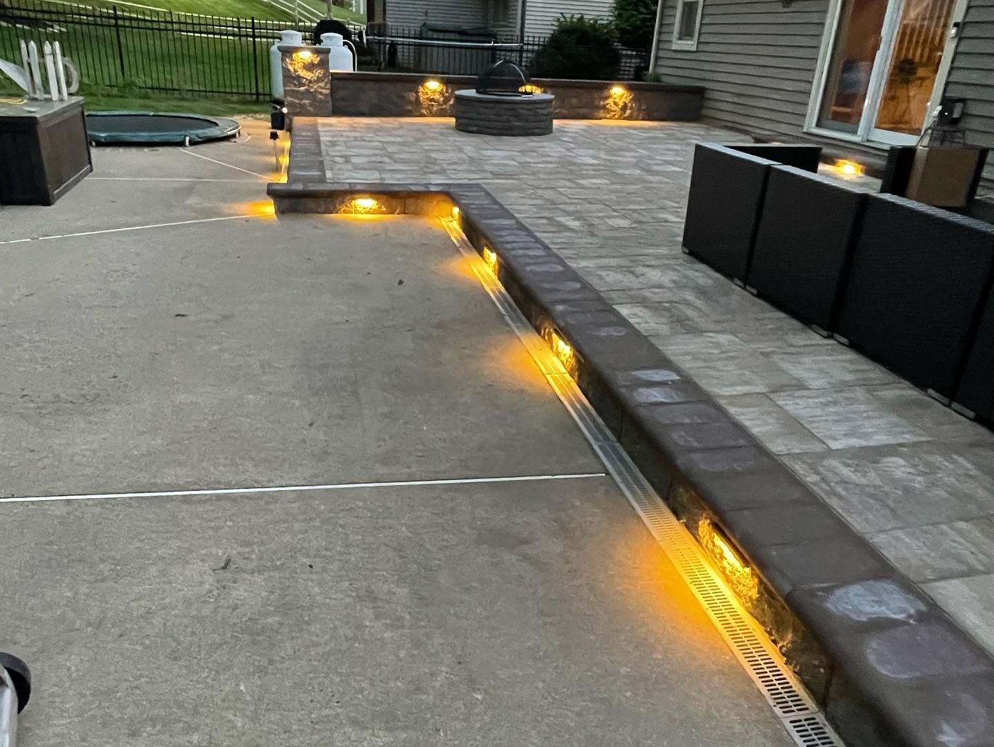 Outdoor patio with brick borders and in-ground lighting illuminating a seating area.