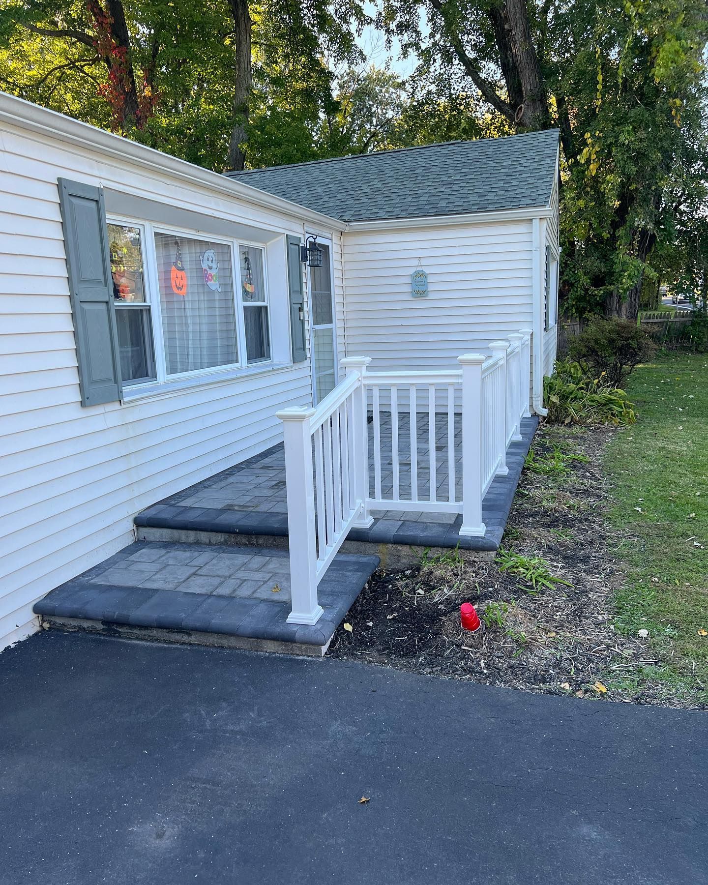 White house entrance with steps and white railing. Asphalt driveway on the right. Green roof and shutters.