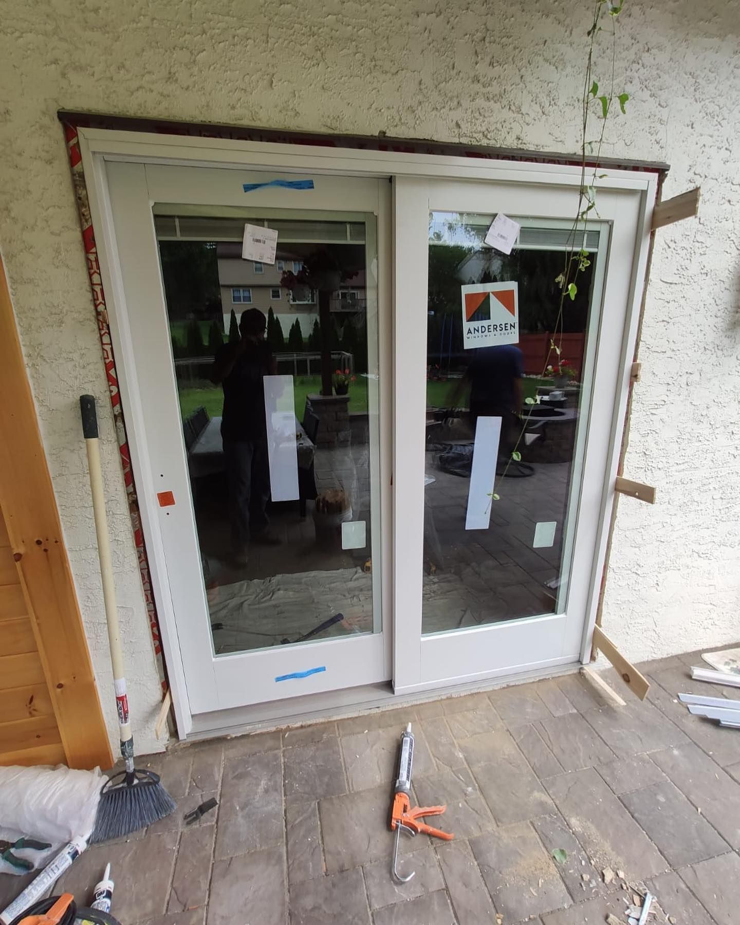 Sliding glass doors partially installed in a white frame, wooden deck. Caulking gun and debris present.