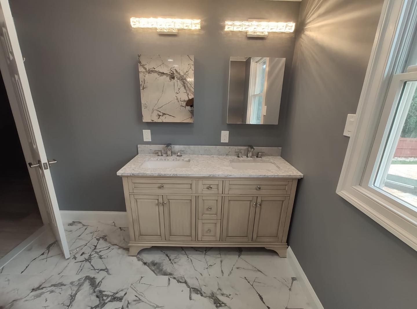 Bathroom with double vanity, marble-look floor and countertop, gray walls, two mirrors, and overhead lights.