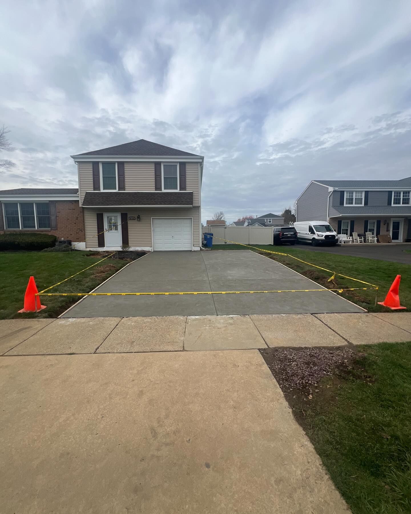 A house with a newly paved driveway blocked by yellow caution tape and orange cones.