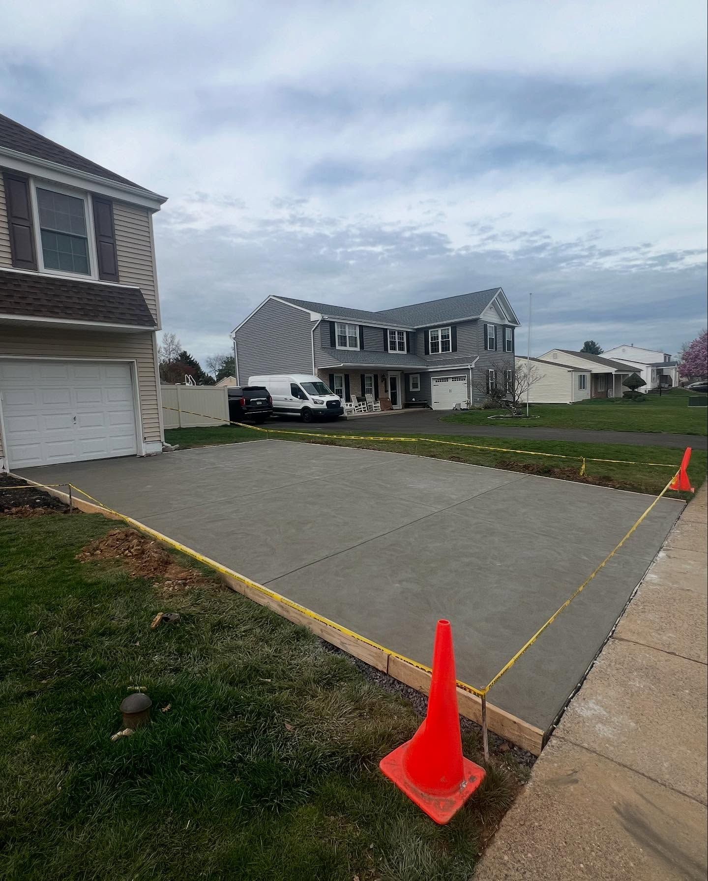 New concrete driveway being constructed in front of a house, with orange traffic cones and wooden borders.