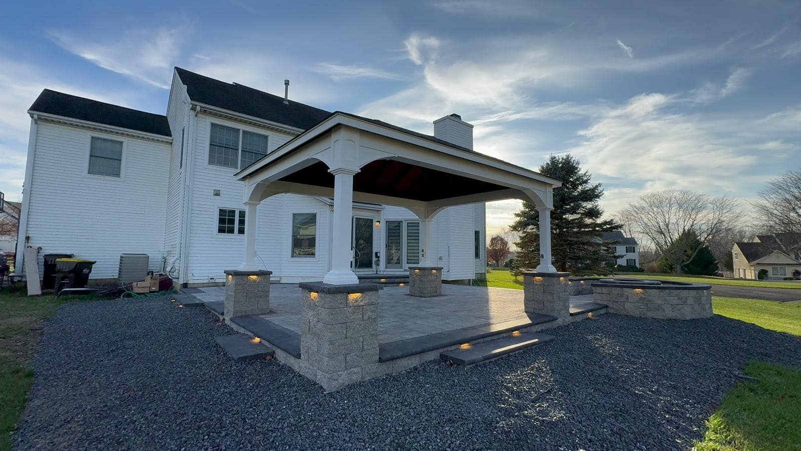 Backyard patio with covered seating, stone features, and a two-story house.