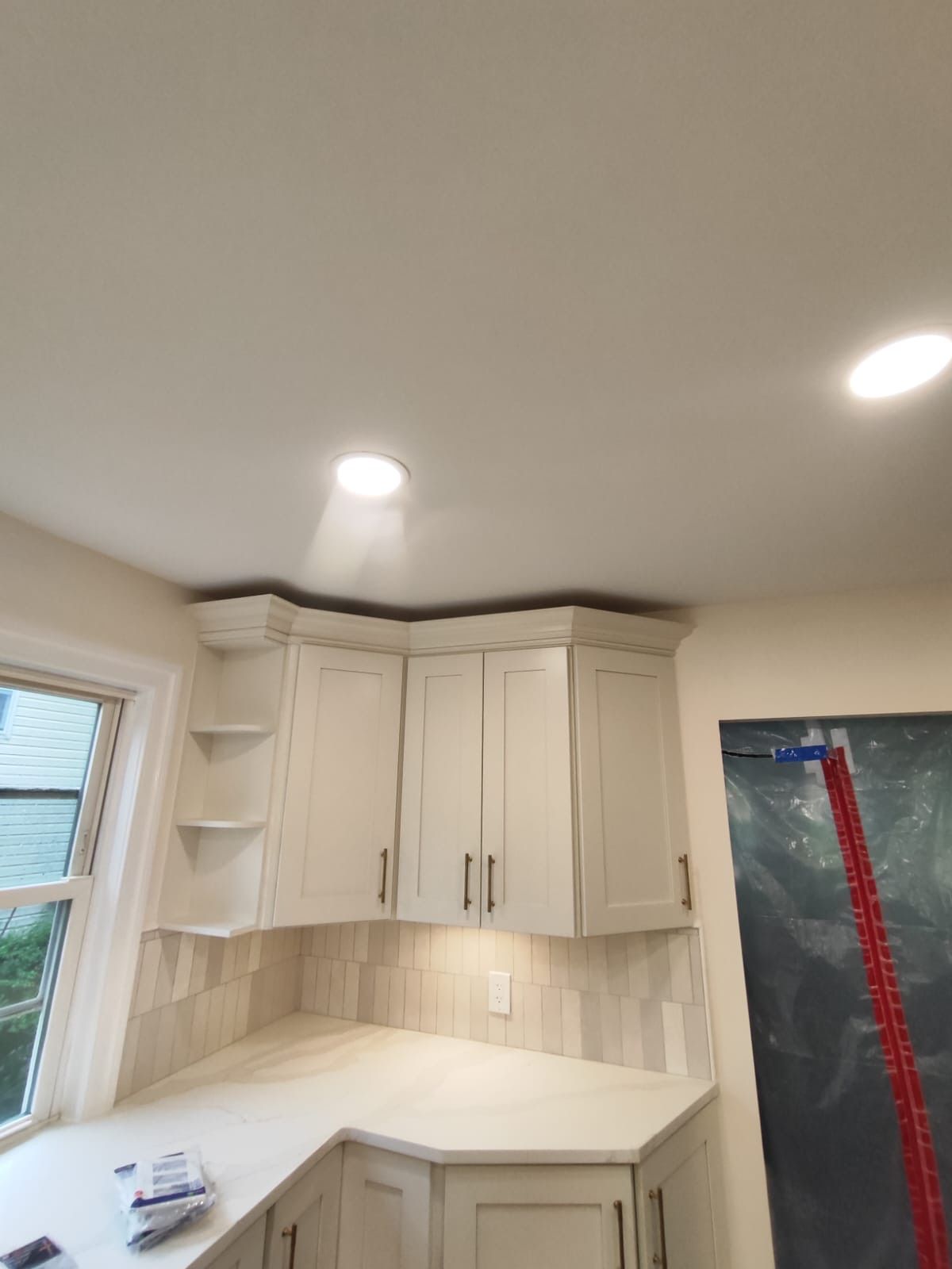 Corner kitchen cabinets with white countertops and tile backsplash; recessed lighting.
