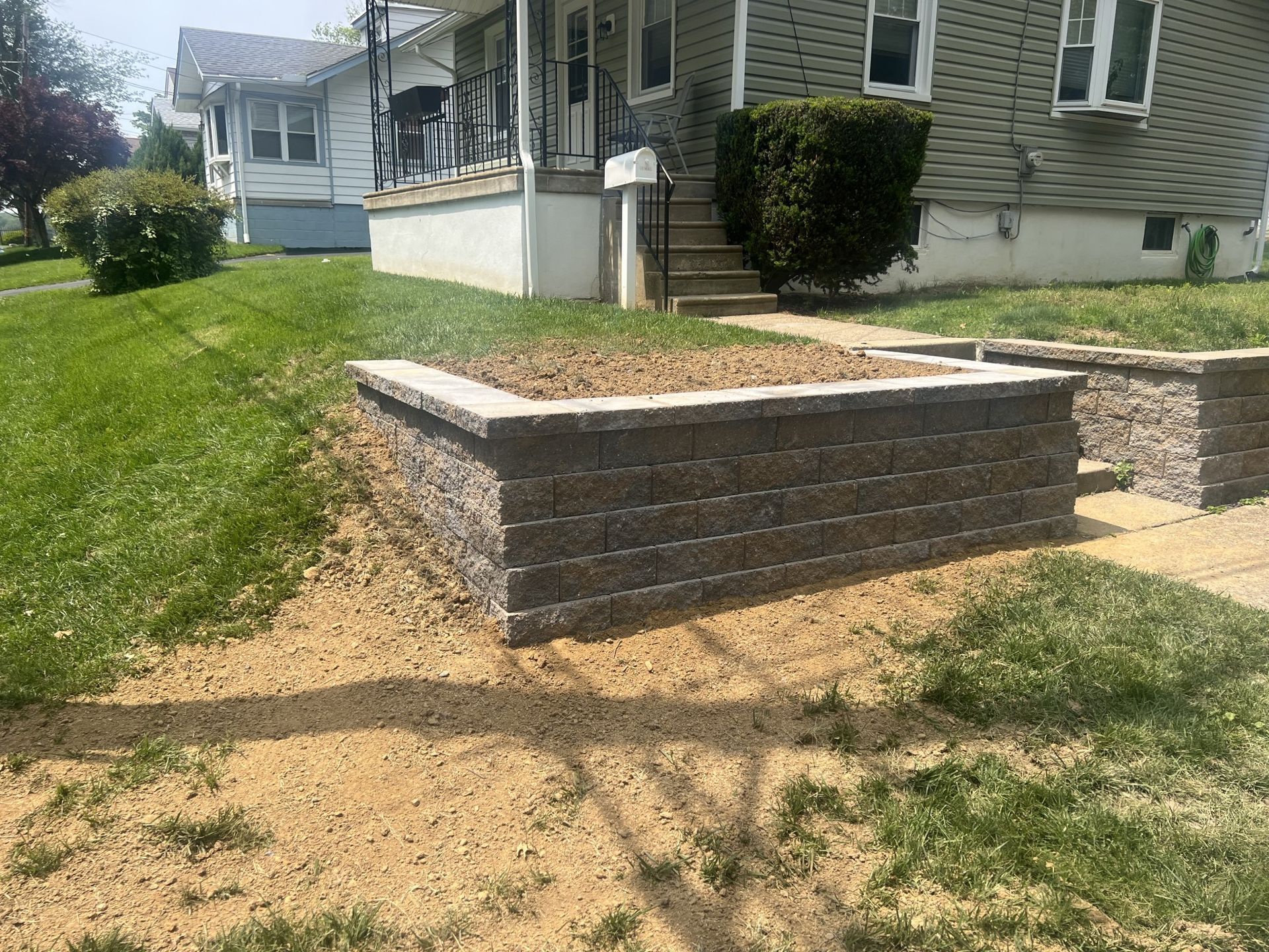 Stone retaining wall in front yard, holding mulch. Green grass and house in background.