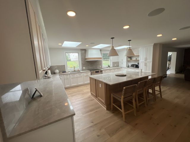 Spacious kitchen with a large island, wooden floors, skylights, and white cabinets.