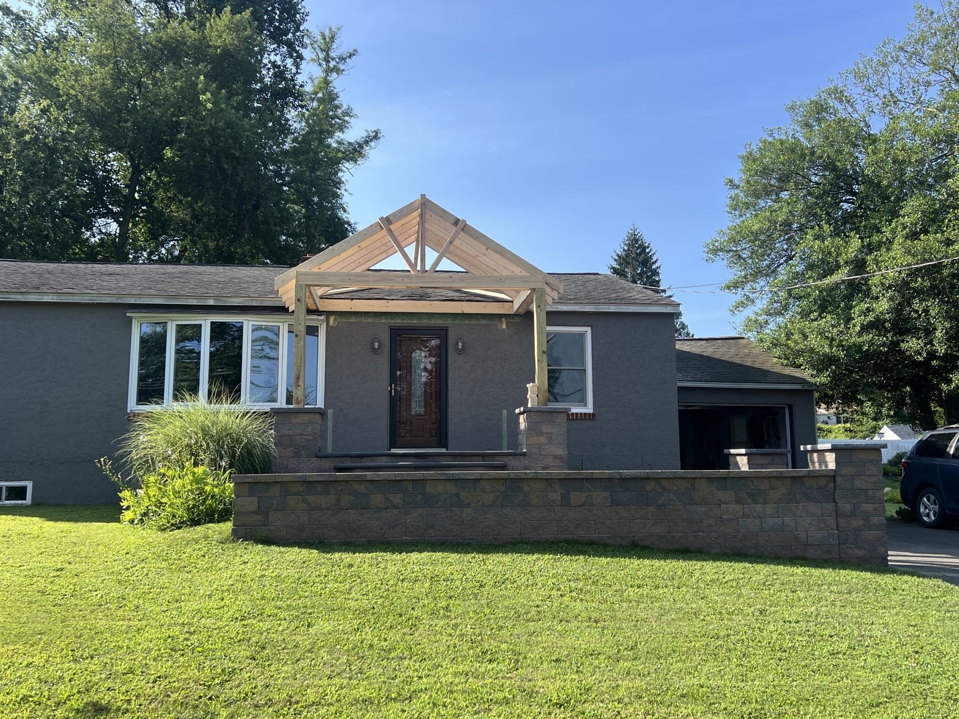 Gray house with a new wooden canopy over the front door, brick retaining wall in the foreground.
