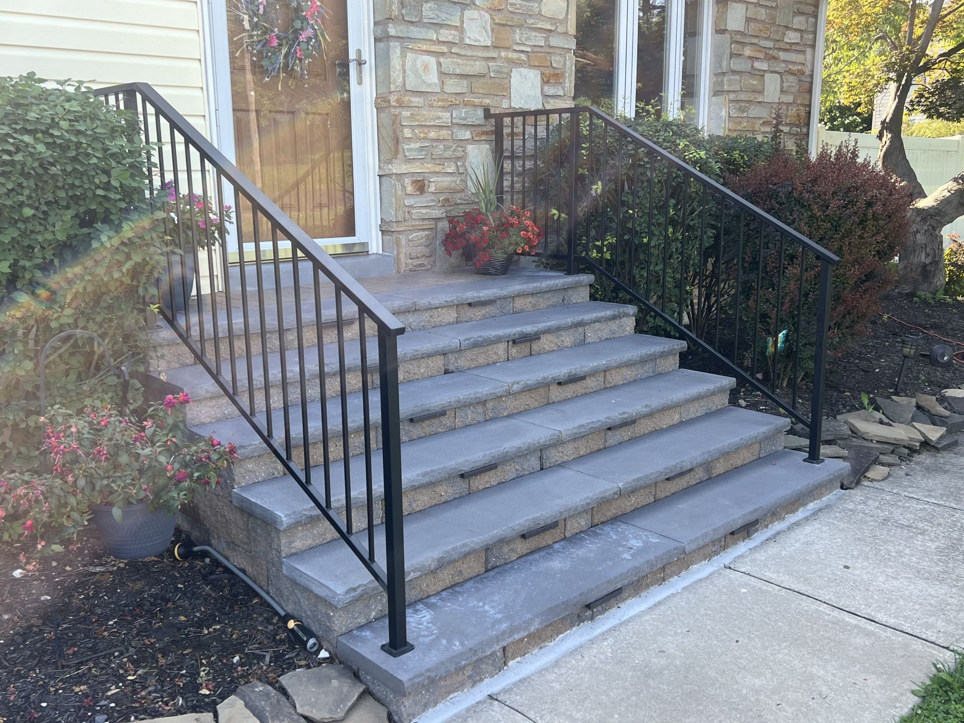 Stone steps leading up to a house entrance, flanked by black metal railings and greenery.