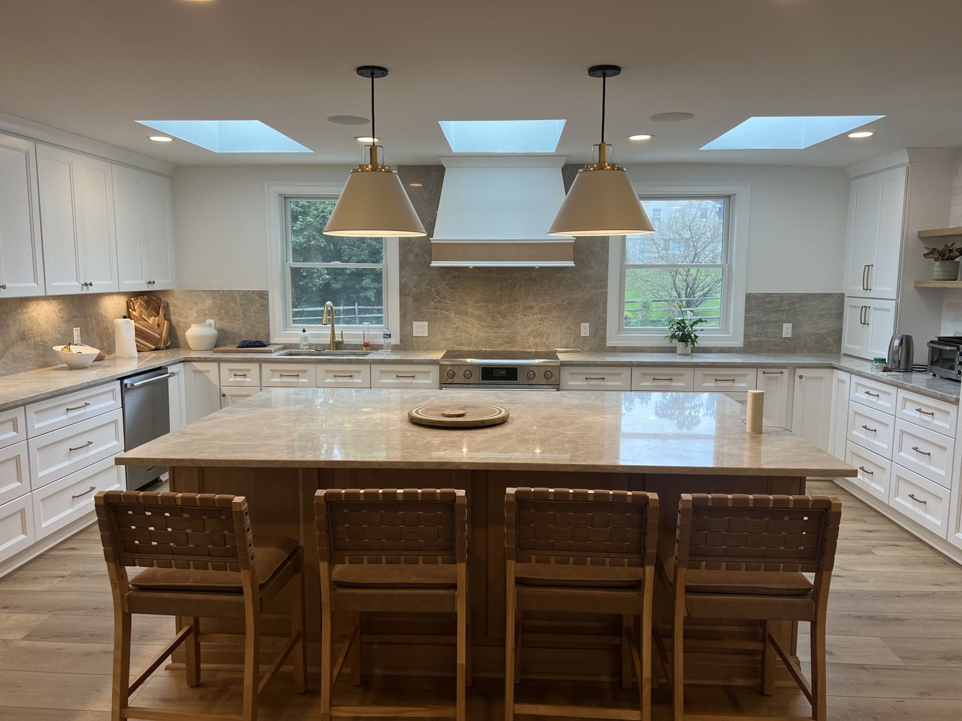 Spacious white kitchen with island, pendant lights, marble countertops, and four barstools.