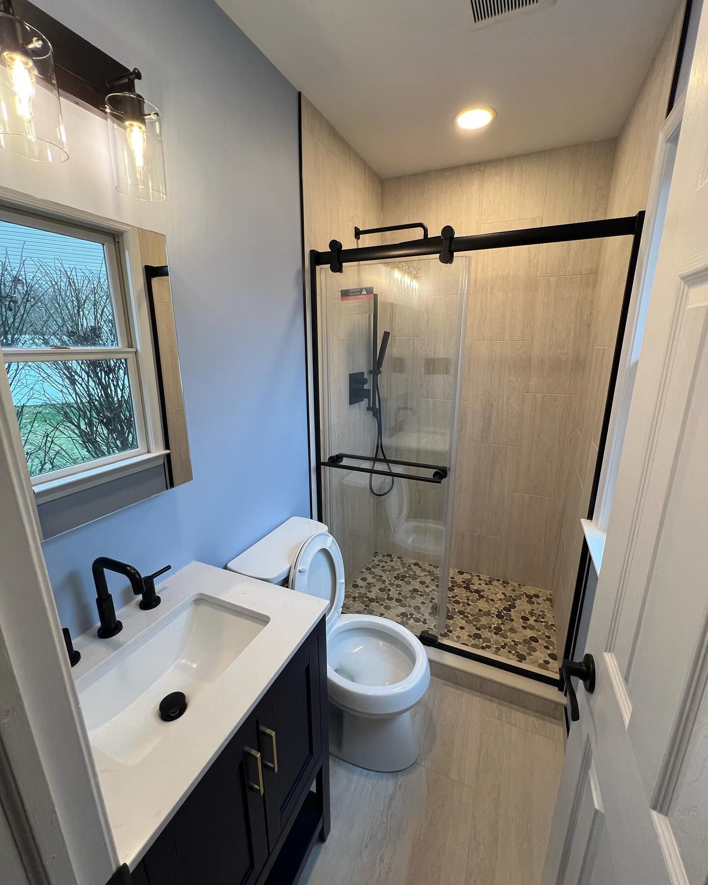 Small bathroom with blue walls, black fixtures, and a glass shower.