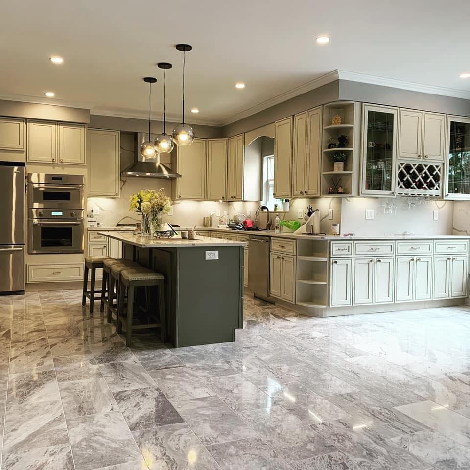 Spacious kitchen with gray marble floors, light cabinets, and a dark green island.