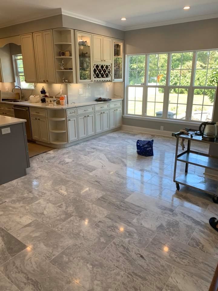 Spacious kitchen with cream cabinets, large windows, and grey marble-like flooring. A blue bag sits on the floor.
