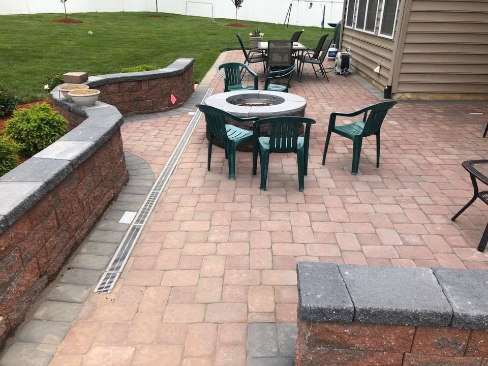 Brick patio with fire pit, seating, and retaining wall along lawn.