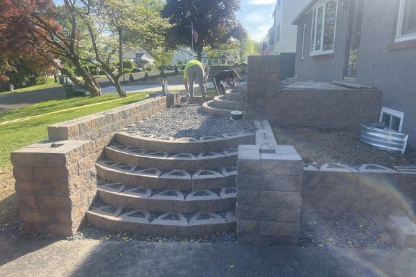 Stone steps and retaining walls being constructed near a house; two workers are present.
