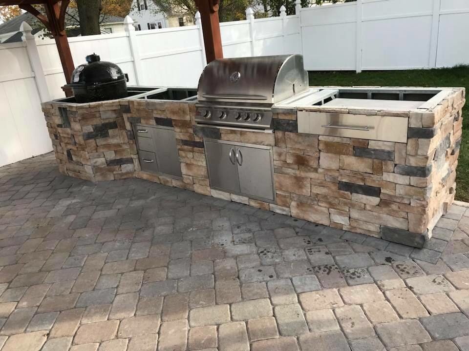 Outdoor kitchen with stone veneer and stainless steel grill, on a brick patio.