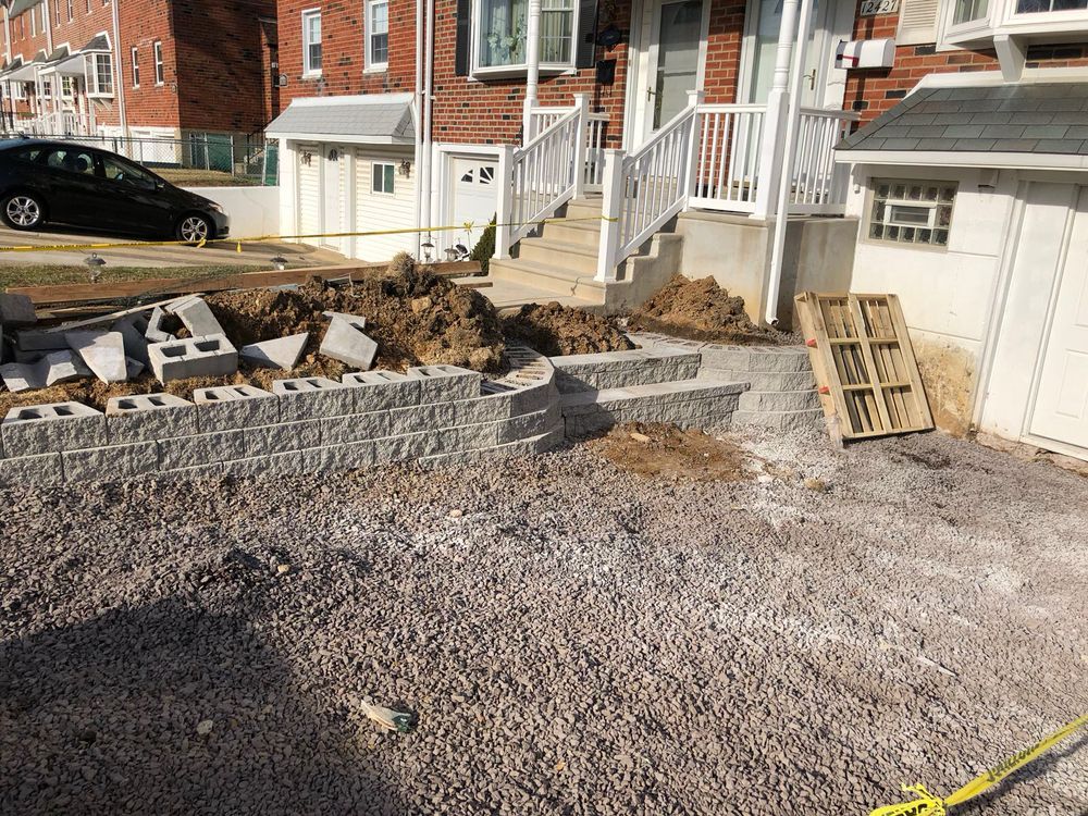 A retaining wall made of gray blocks is under construction in front of a house.