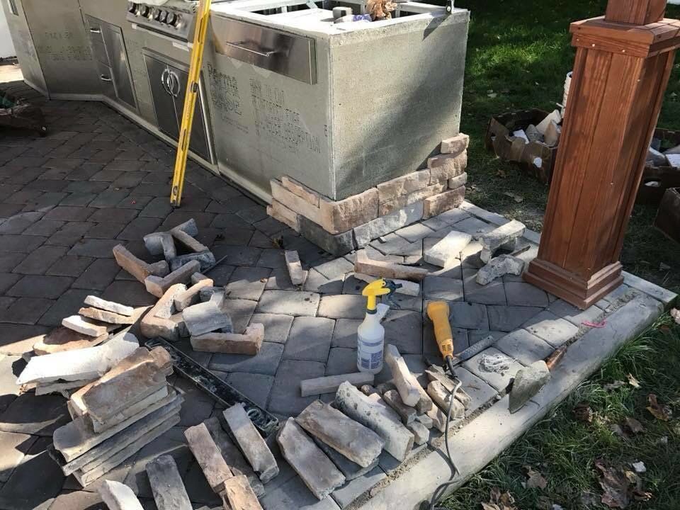 Outdoor kitchen under construction; bricks, tools, and a wooden post are visible.