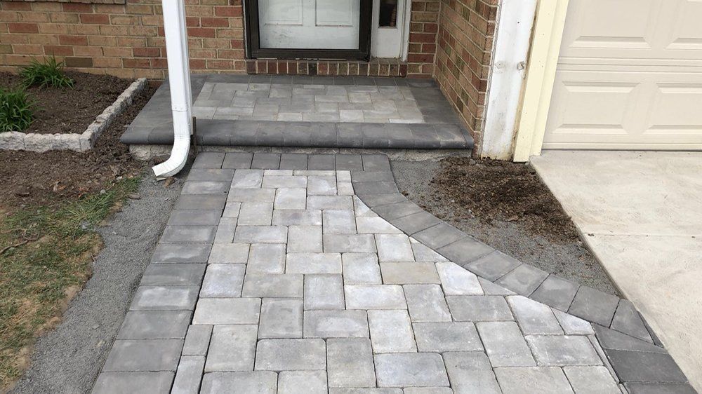 Brick paver walkway leading to a front door and porch with brick facade and gutter.