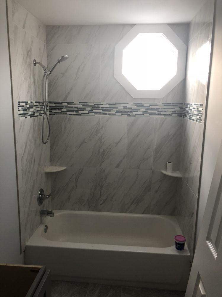 Newly renovated shower with white and gray marble-like tiles, a decorative band, and an octagonal window.