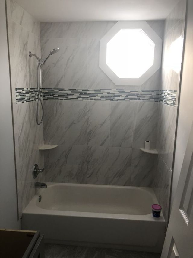 Newly renovated shower with white and gray marble-like tiles, a decorative band, and an octagonal window.