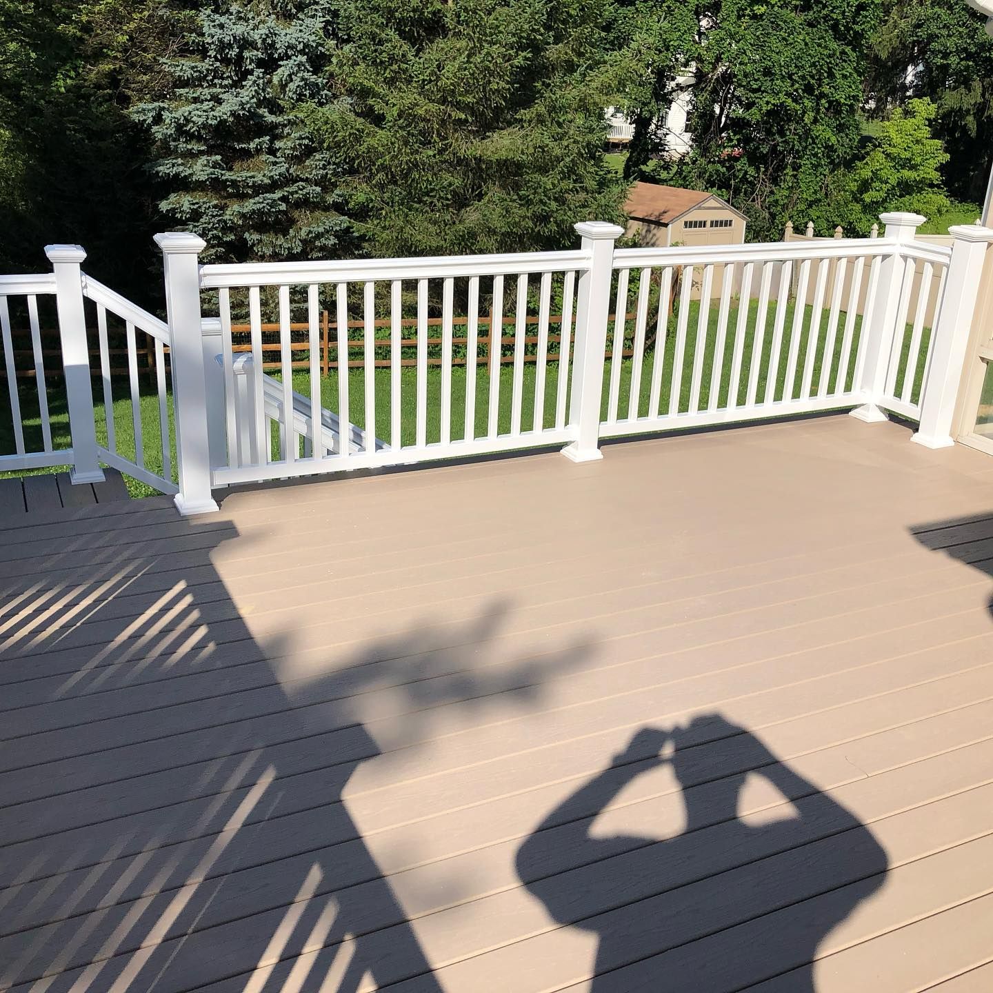Beige deck with white railing in a backyard with trees.