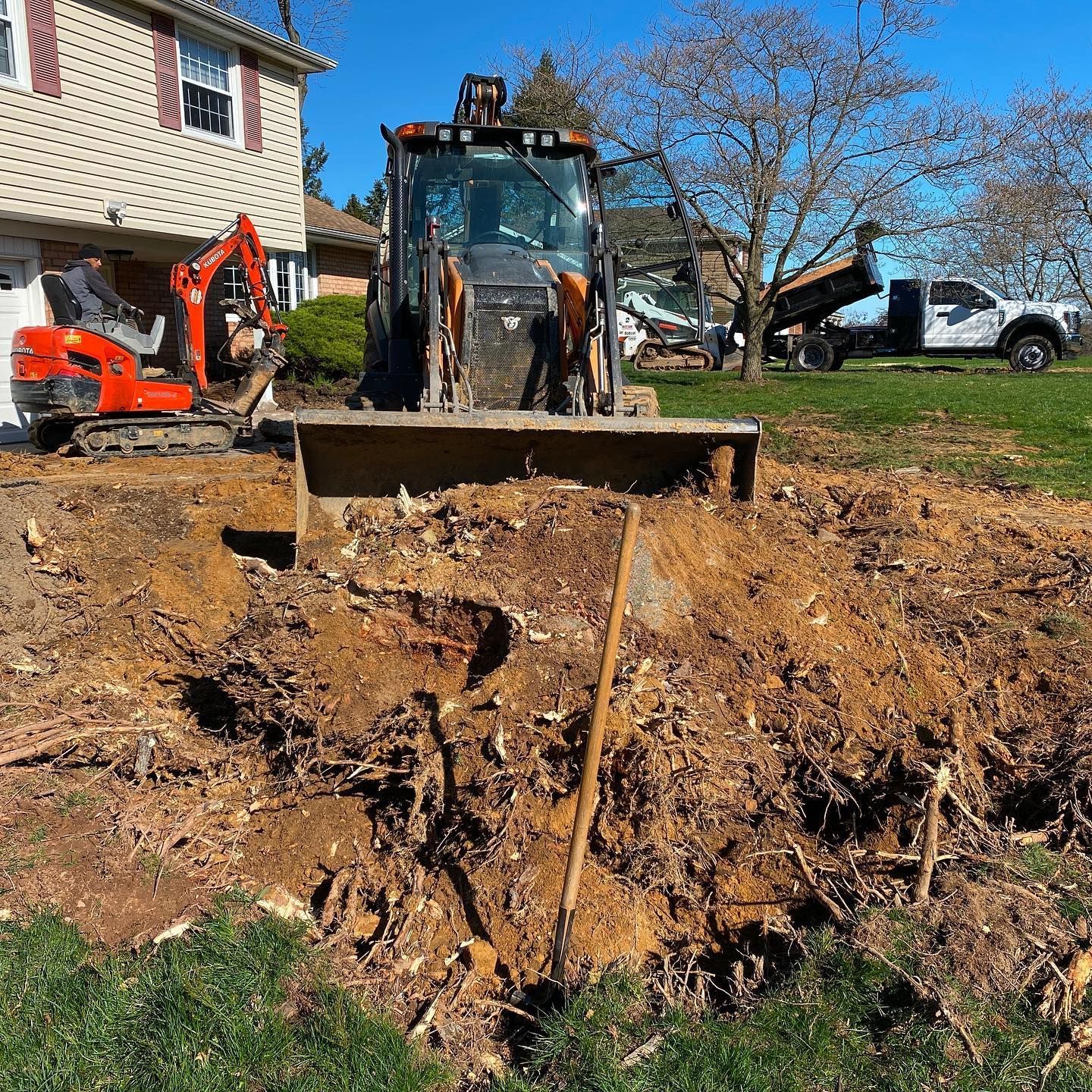 Construction site with excavator and backhoe removing tree stump in front yard.