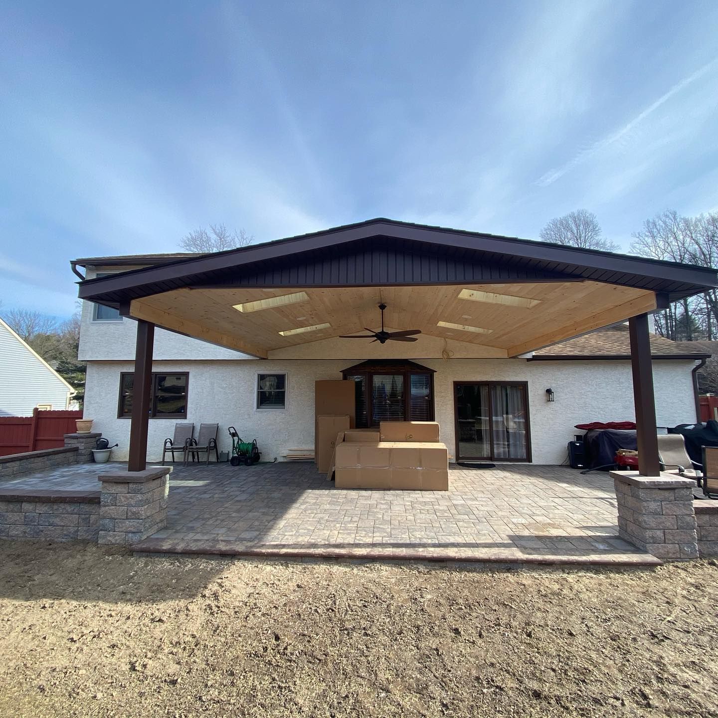 Backyard patio with a large covered structure, brown trim, and a ceiling fan.