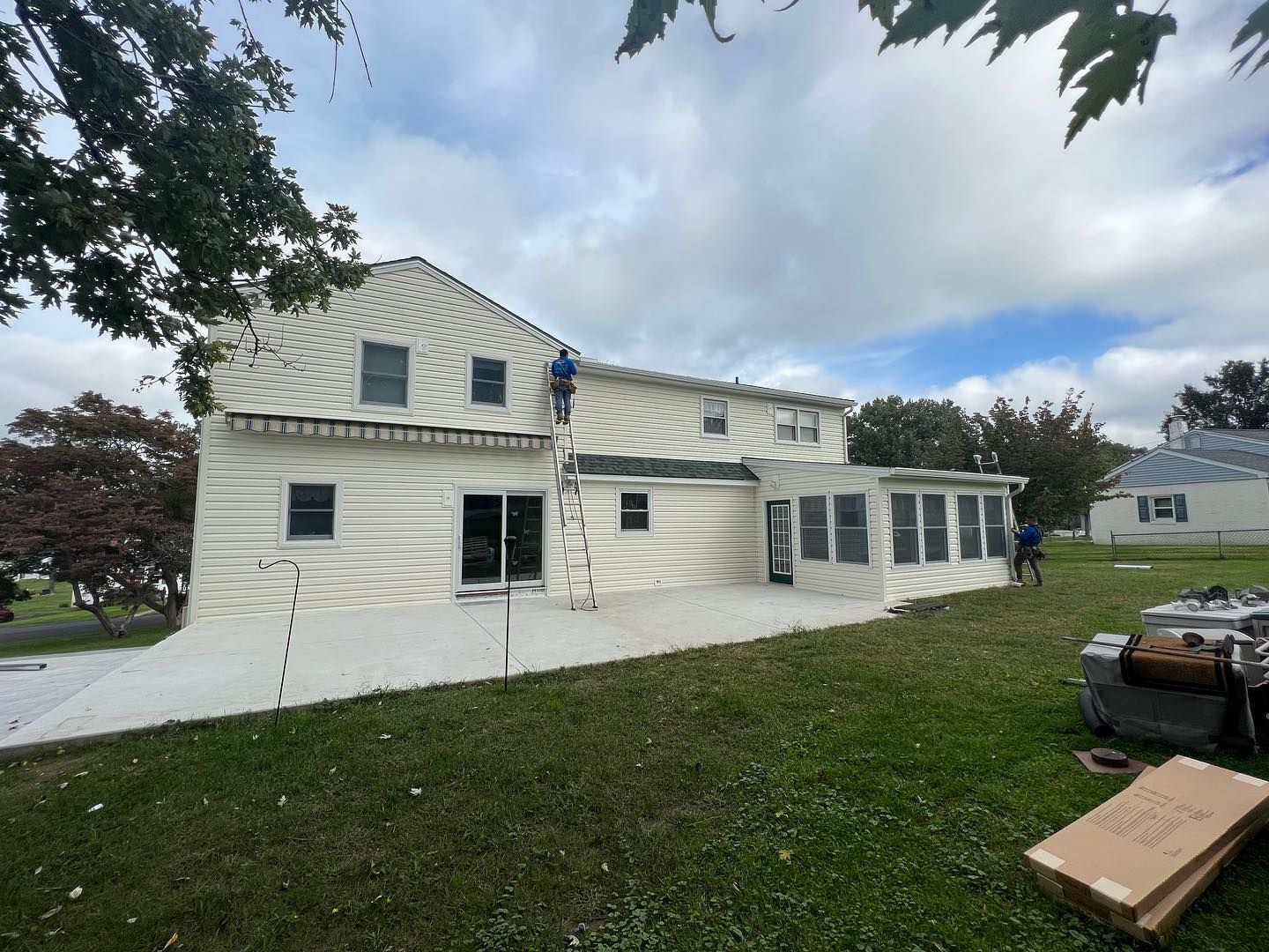 House being worked on with siding, a ladder, and workers. Sunny day with green lawn.