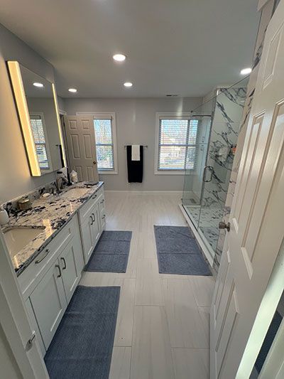 Bathroom with white cabinets, marble shower, and gray bath mats.