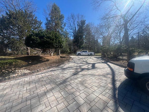 Paver driveway with a white pickup truck, surrounded by trees under a bright blue sky.