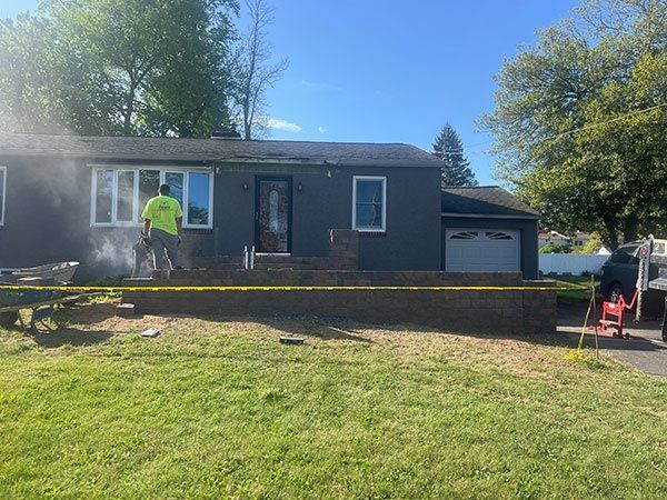 House exterior with construction in progress. Brickwork, yellow caution tape, worker, blue house, green lawn.