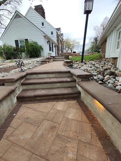 Stone path with steps leading toward a white building. Low lighting and rock garden on the sides.