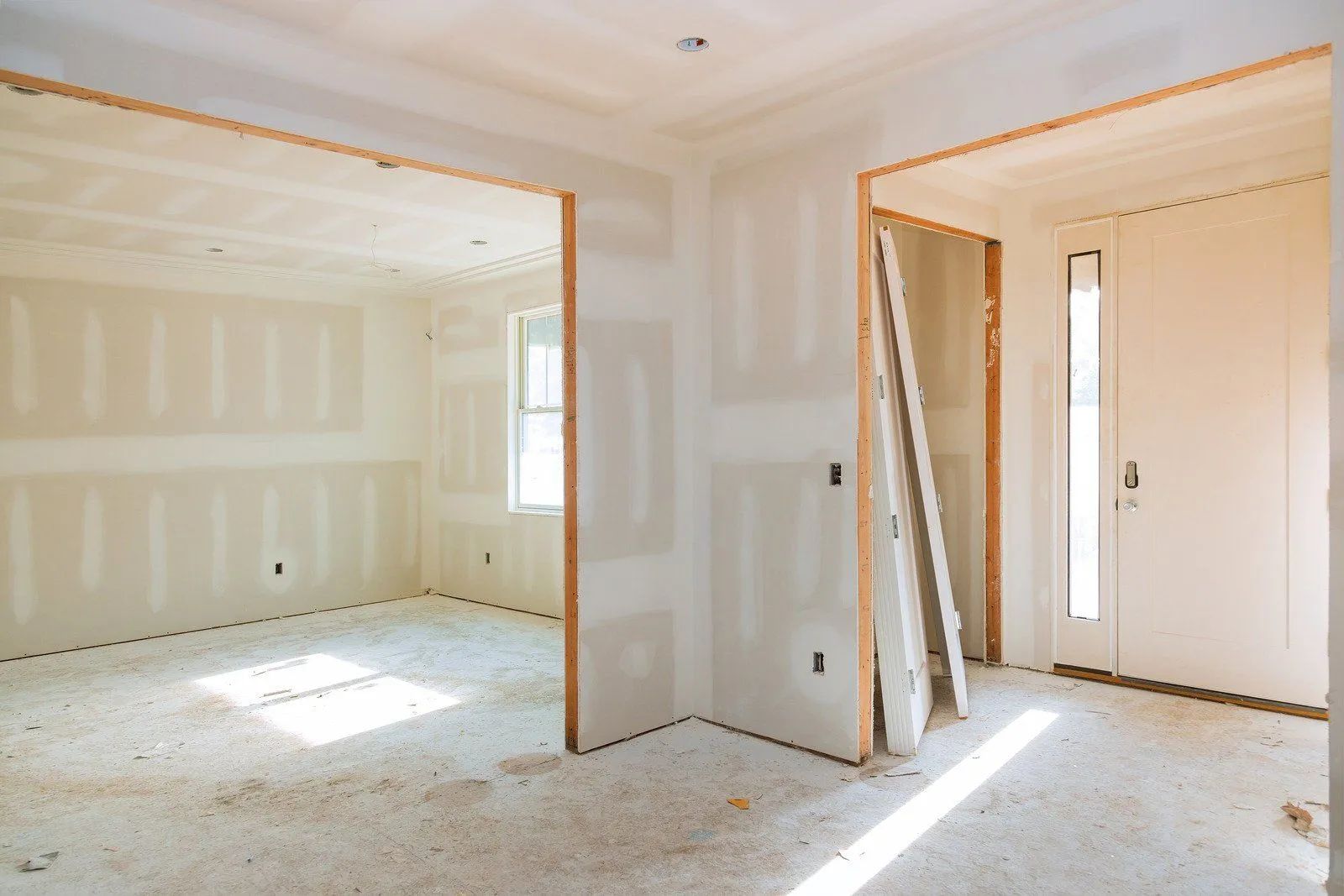 Empty unfinished room with drywall, exposed doorways, and sunlight streaming across the floor.