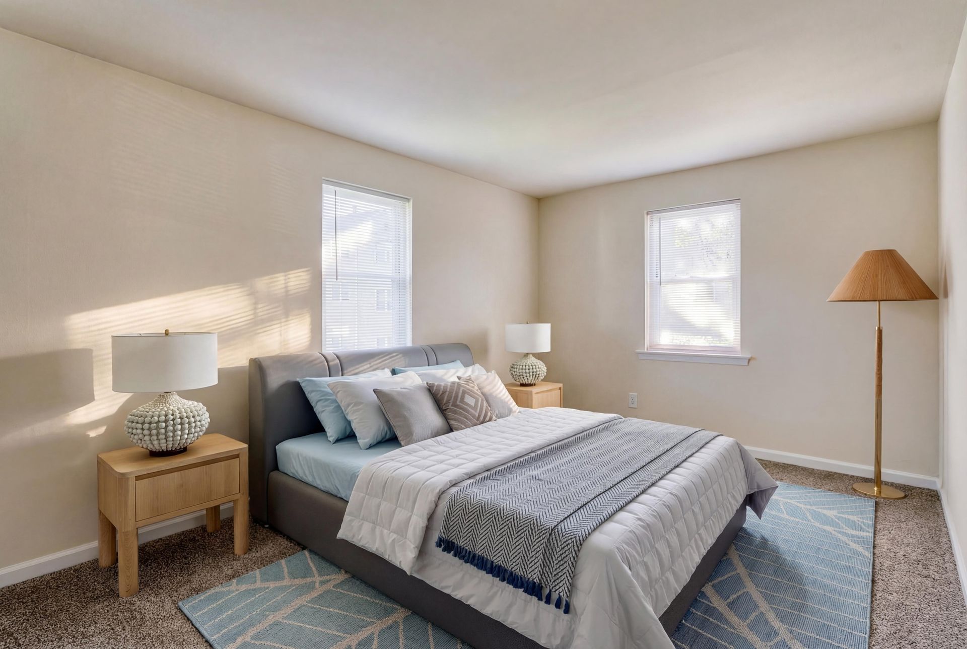 Brookbend Apartments Neutral bedroom with a queen bed, two wooden nightstands, and a floor lamp in a well-lit apartment.