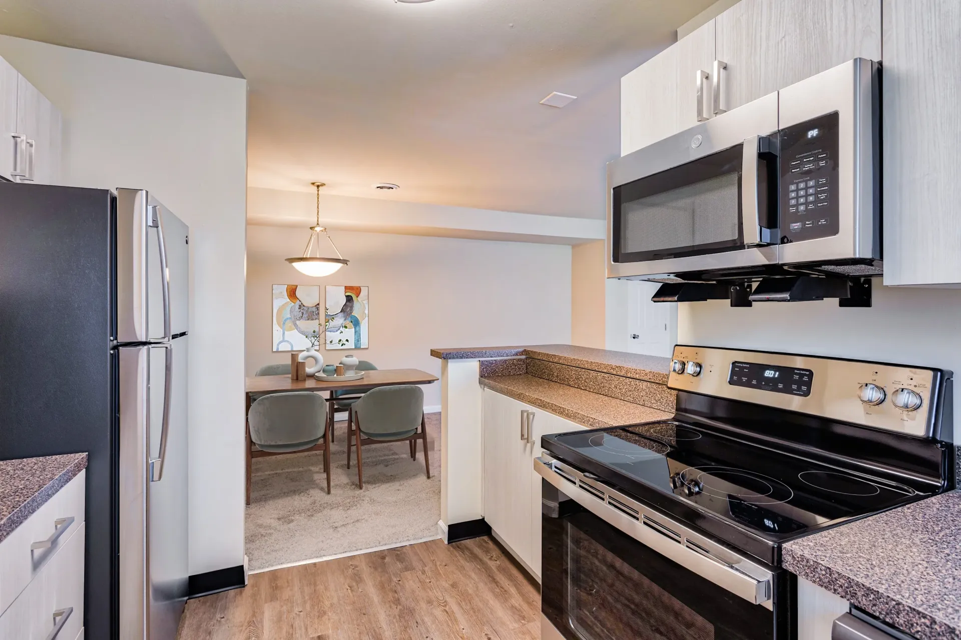 Brookbend Apartments Modern kitchen with stainless steel fridge, microwave, and stove; dining area visible in an open-plan space.