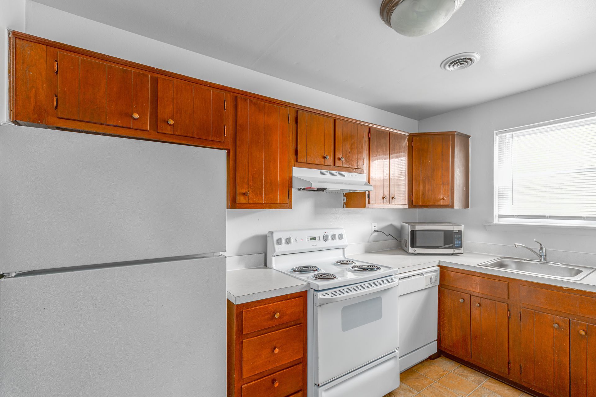 Brookbend Apartments Kitchen with white appliances, wooden cabinets, and a window.