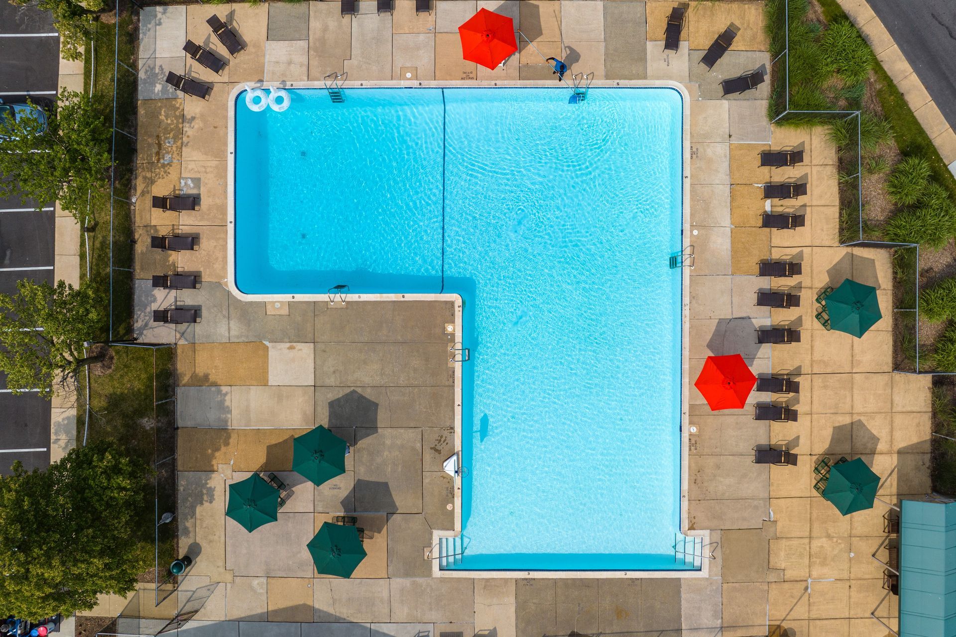 Brookbend Apartments Aerial view of an L-shaped swimming pool with people, umbrellas, and lounge chairs. Bright blue water.