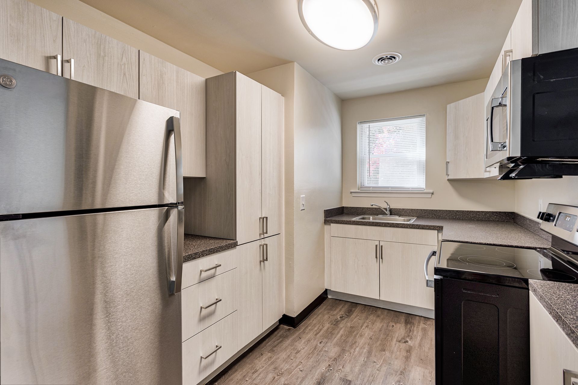 Brookbend Apartments Kitchen with stainless steel refrigerator, white cabinets, dark countertops, and a window.