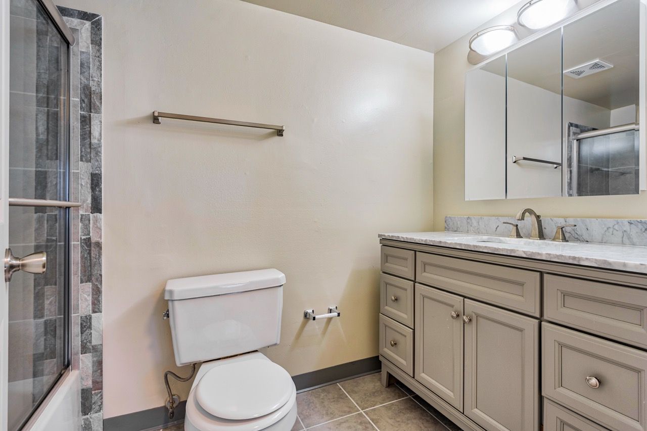 Brookbend Apartments Bathroom with toilet, marble countertop vanity, and glass-enclosed shower.