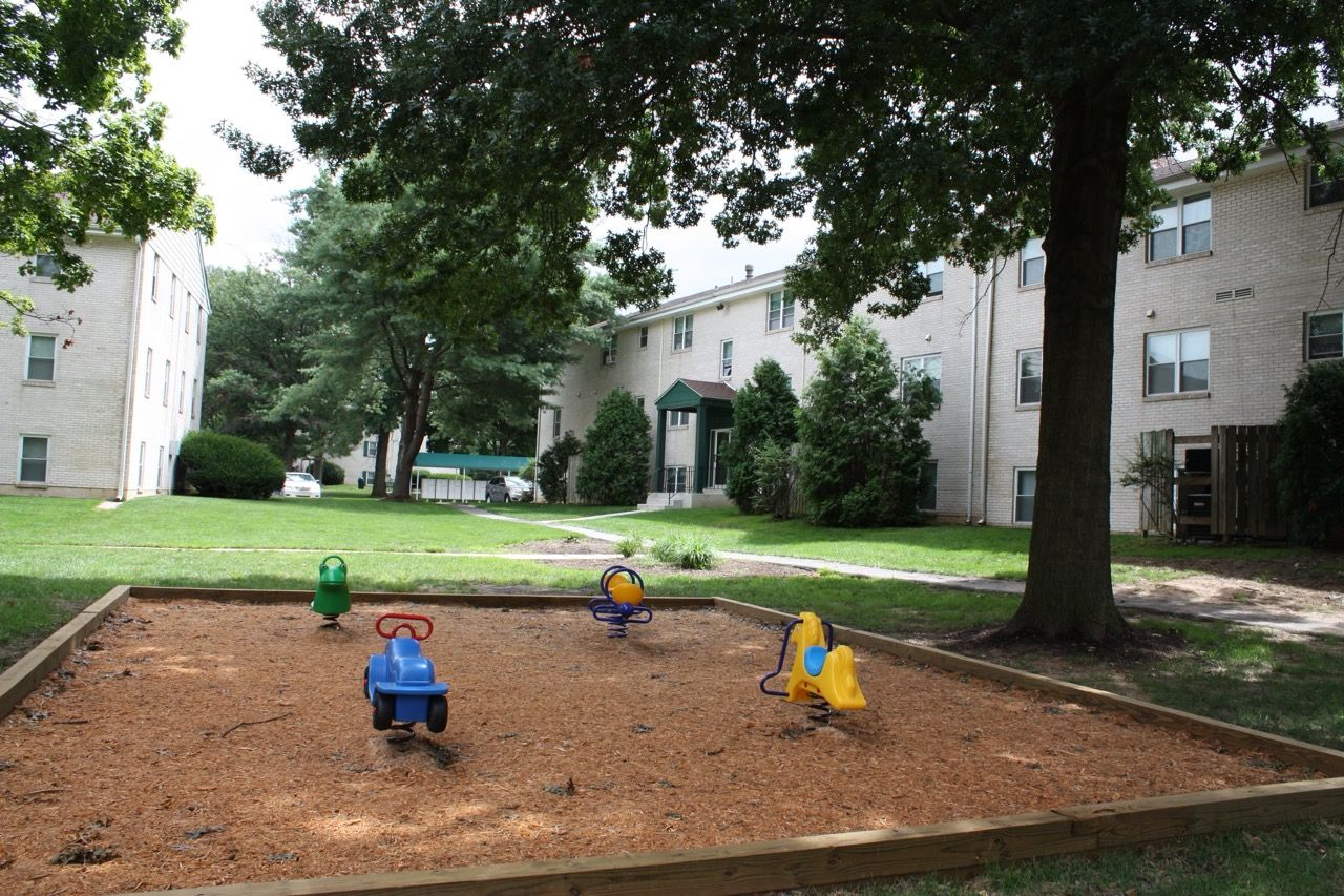 Brookbend Apartments Playground area in a grassy apartment complex courtyard with mulch and small ride-on toys.