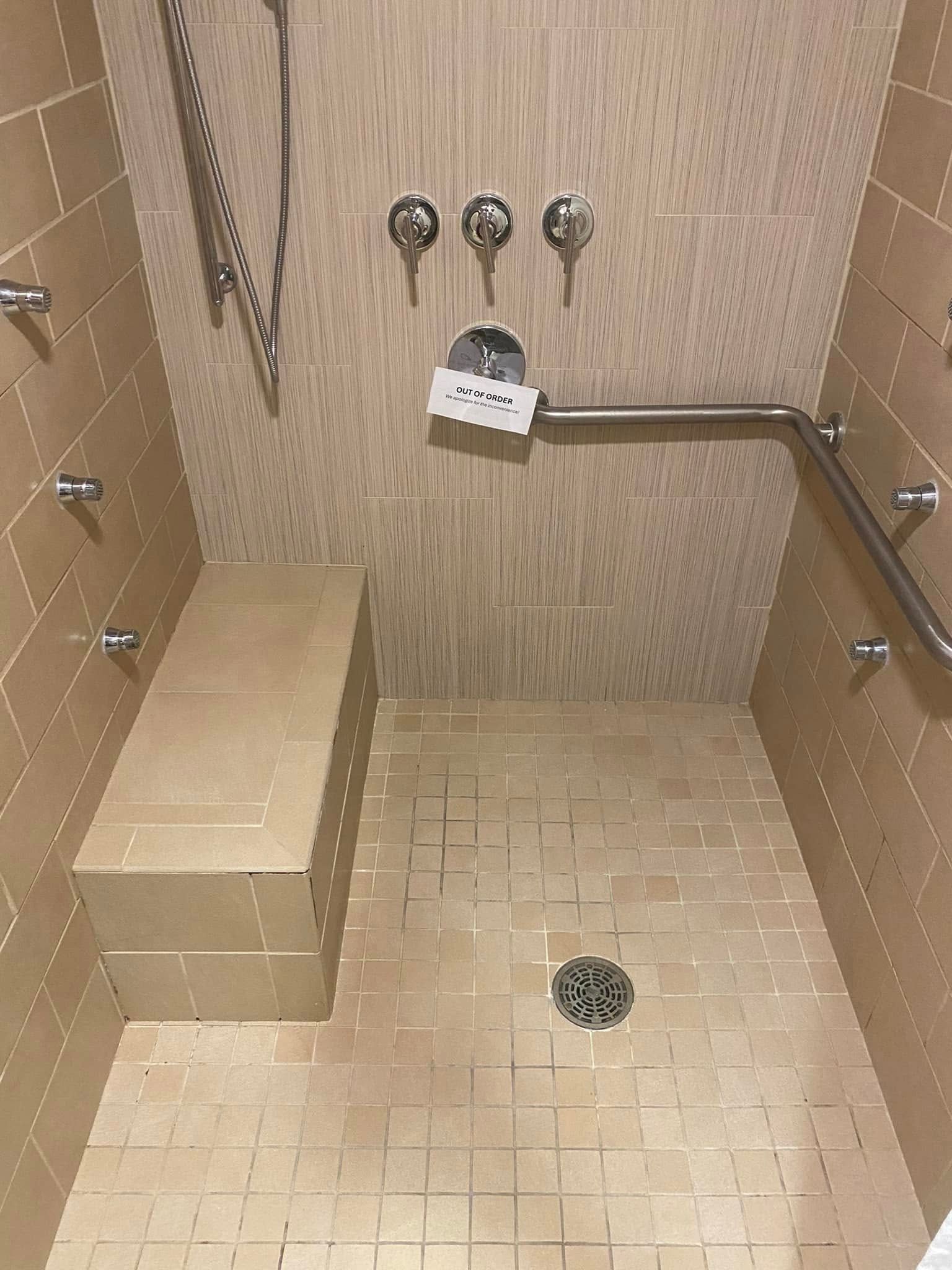 Accessible shower with built-in bench, grab bar, multiple shower heads, and tiled walls/floor.