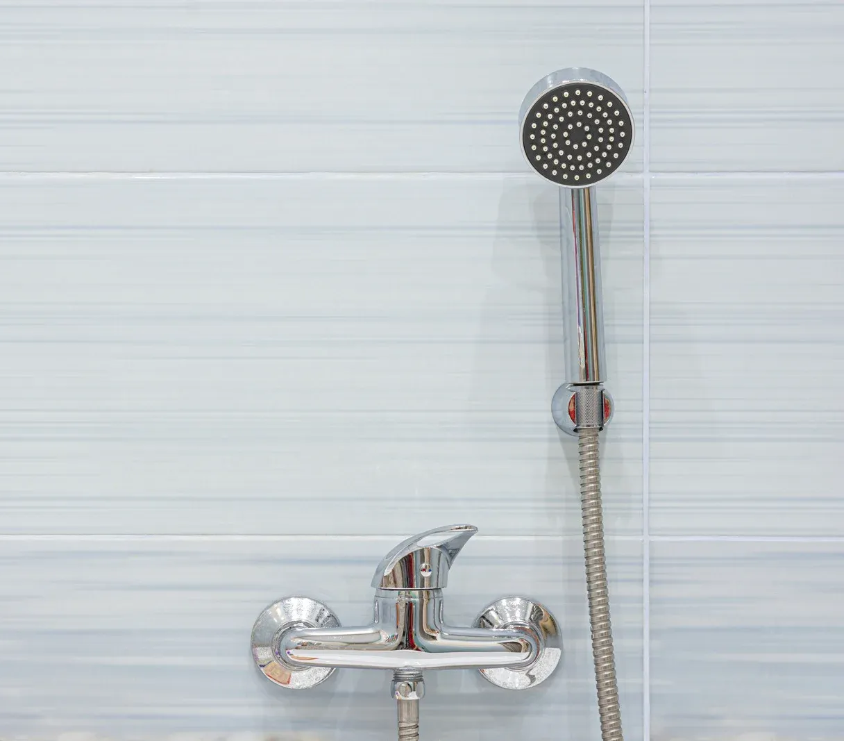 Showerhead and faucet against light blue tiled wall.