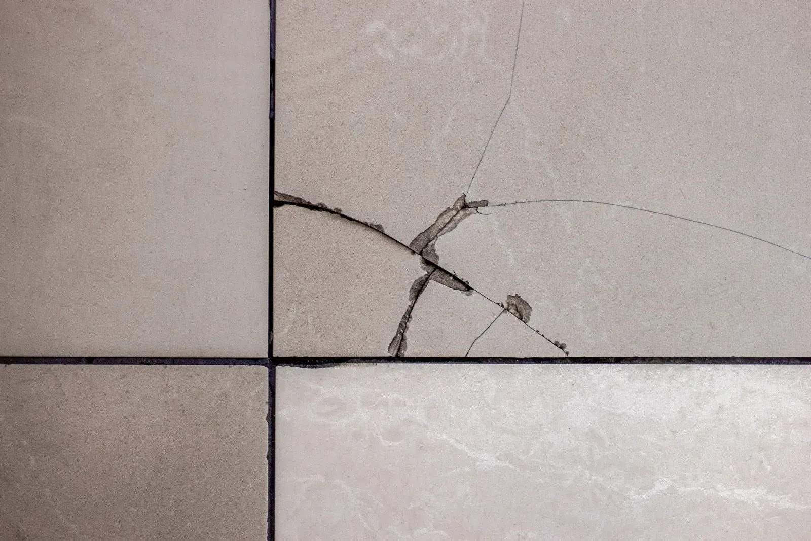 Cracked beige tile with black grout lines.