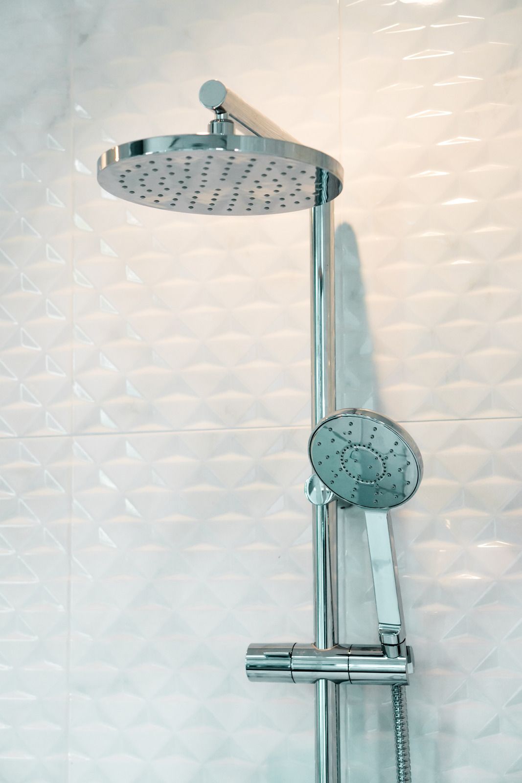 Chrome shower head with handheld shower on a white tiled wall.
