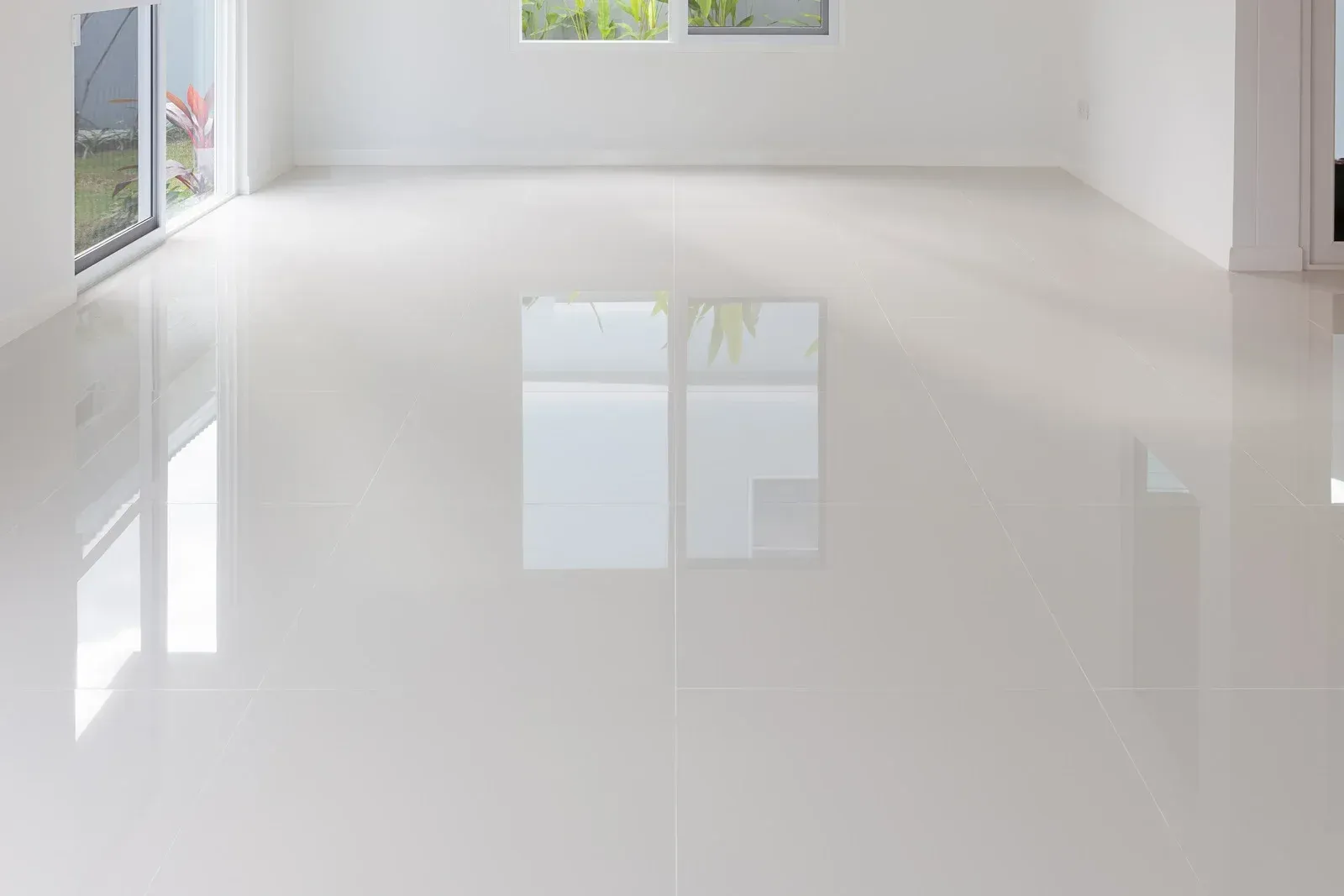Empty room with glossy white floor, walls, and windows reflecting light.