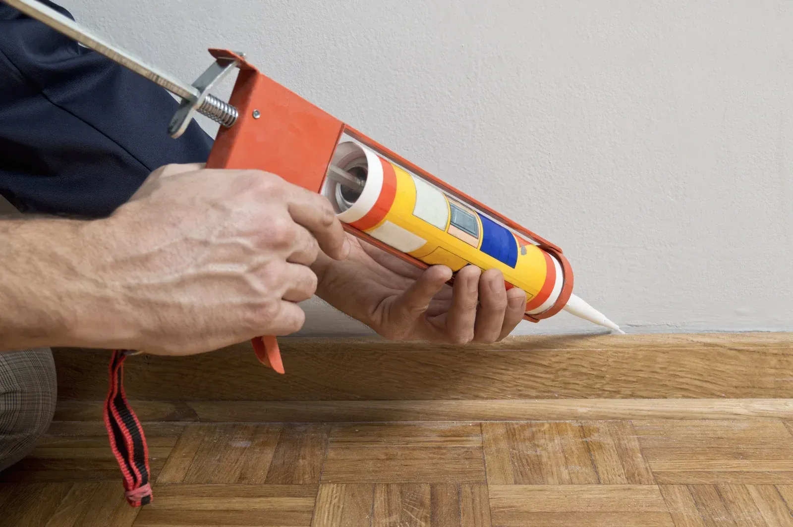 Person caulking baseboard with orange caulk gun.